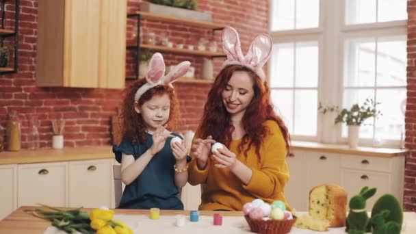 A mother and her daughter painting Easter eggs in cozy kitchen. They laughing and have fun. Happy family preparing for Easter. Happy easter — Stock Video