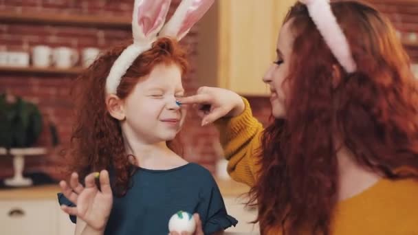 Feliz Pascua. La joven madre y su hijita se pintan huevos y rostros. Chistes familiares — Vídeo de stock
