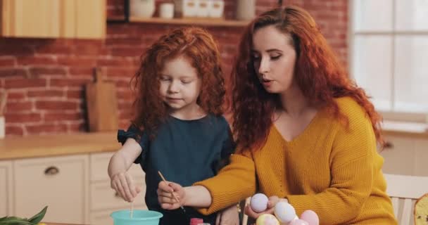 Мать с дочерью рисуют пасхальные яйца на уютной кухне. Они смеются и веселятся. Счастливая семья готовится к Пасхе. Счастливой Пасхи — стоковое видео
