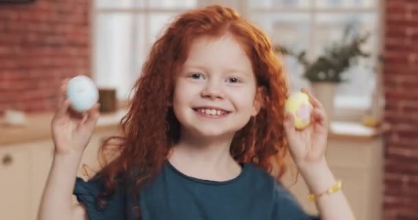 Retrato de niña pelirroja alegre jugando con huevo de Pascua en el fondo de la cocina. Ella está animando y divirtiéndose en la cámara. Feliz Pascua — Vídeos de Stock