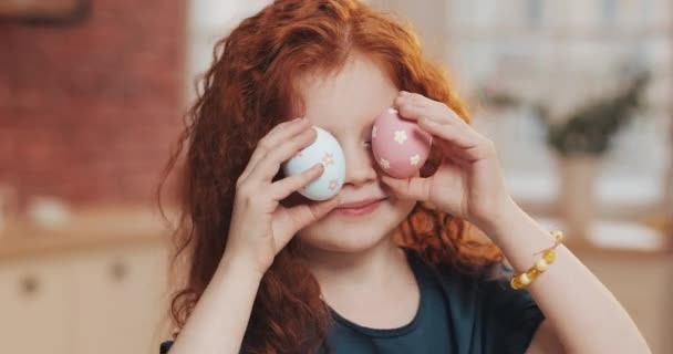 Retrato de menina ruiva alegre criança brincando com ovo de Páscoa no fundo da cozinha. Ela está aplaudindo e se divertindo com a câmera. Feliz Páscoa — Vídeo de Stock