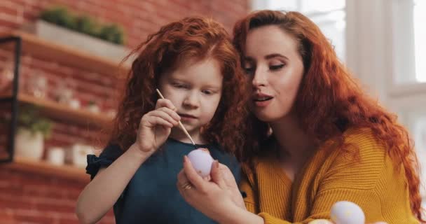 Una madre y su hija pintando huevos de Pascua en la acogedora cocina. Se ríen y se divierten. Familia feliz preparándose para la Pascua. Feliz Pascua. — Vídeos de Stock