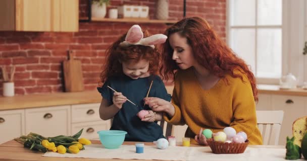 Feliz Páscoa. A mãe ensina a filha a pintar ovos. Família feliz se preparando para a Páscoa. Menina usando orelhas de coelho — Vídeo de Stock