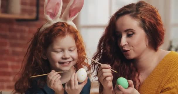 Gledelig østlig. Mor og hennes lille datter maler egg. Lykkelig familie forbereder påske. De har kaninører. – stockvideo
