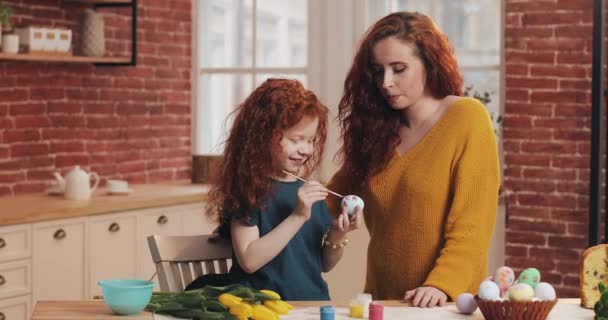 Feliz Pascua. Mamá enseña a su hija a pintar huevos. Familia feliz preparándose para la Pascua. Niña usando orejas de conejo — Vídeo de stock