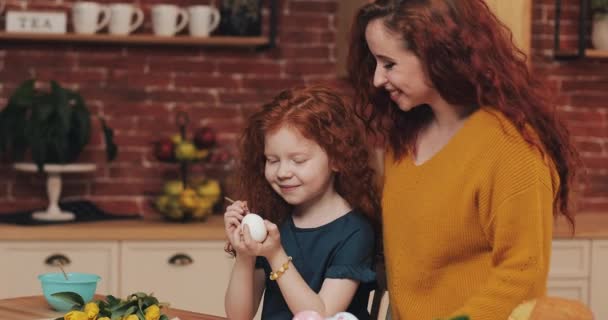 Feliz Pascua. Mamá enseña a su hija a pintar huevos. Familia feliz preparándose para la Pascua. Niña usando orejas de conejo — Vídeo de stock