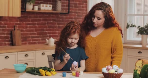 Feliz Pascua. Mamá enseña a su hija a pintar huevos. Familia feliz preparándose para la Pascua. Niña usando orejas de conejo — Vídeo de stock