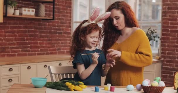 Joyeuse Pâques. Maman enseigne à sa fille à peindre des œufs. Bonne famille se préparant pour Pâques. Petite fille portant des oreilles de lapin — Video