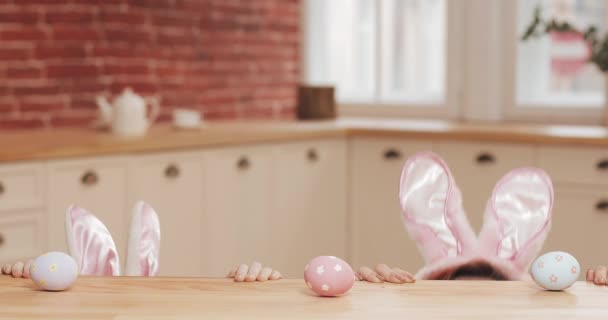 Feliz Pascua. La joven madre y su hija comienzan a cazar huevos de Pascua con oreja de conejo. Familia feliz preparándose para la Pascua en la acogedora cocina — Vídeos de Stock