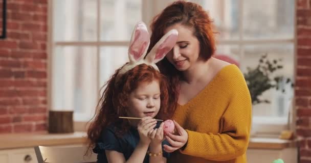 Счастливой Пасхи. Мама учит свою дочь рисовать яйца. Счастливая семья готовится к Пасхе. У них кроличьи уши. — стоковое видео