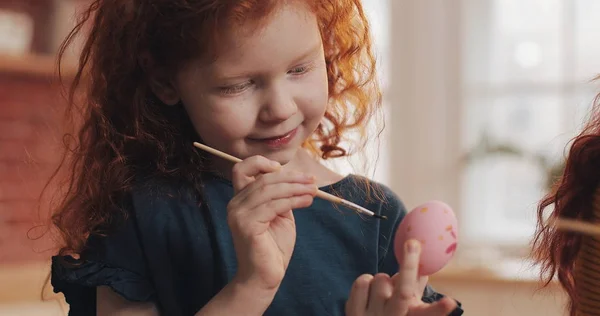 Annesi mutfak arka planına paskalya yumurtası çizen neşeli kızıl saçlı küçük kız. Mutlu Paskalyalar