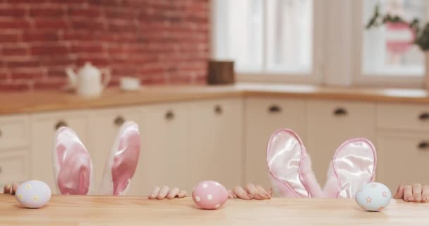 Feliz Pascua. La joven madre y su hija comienzan a cazar huevos de Pascua con oreja de conejo. Familia feliz preparándose para la Pascua en la acogedora cocina — Vídeos de Stock