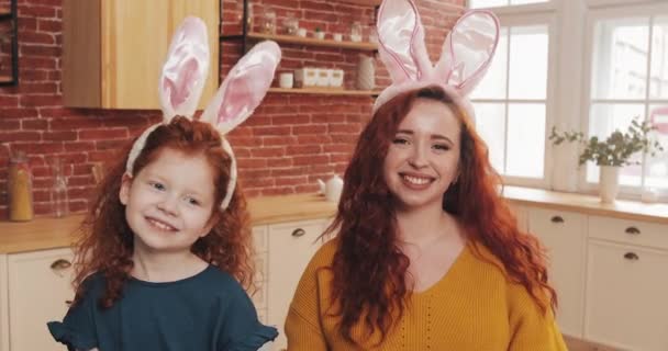 Feliz Pascua. Alegre pelirroja niña con su madre usando oreja de conejito haciendo video chat con familiares o amigos. Agitan las manos, hablan y se divierten en la cámara — Vídeos de Stock