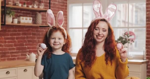Retrato de niña pelirroja alegre con su mamá jugando con huevo de Pascua en el fondo de la cocina. Están animando y divirtiéndose en la cámara. Feliz Pascua — Vídeos de Stock