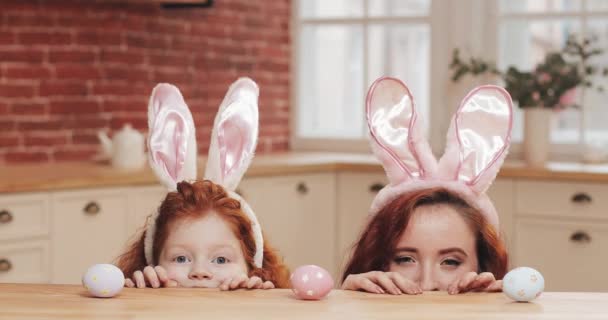 Πορτρέτο της αστείας μαμάς και της κόρης της φορώντας λαγουδάκι αυτί με πασχαλινά αυγά κοιτάζοντας μέσα στην κάμερα. ευτυχισμένη οικογένεια που διασκεδάζει στην άνετη κουζίνα. Καλό Πάσχα. — Αρχείο Βίντεο