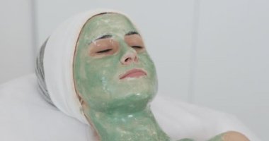 Spa salonda kadın. Yüz maskesi. Güzel kız kanepede içinde kozmetik yeşil bir maske ile yalan Kliniği