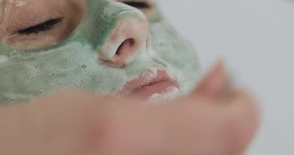 Vacker ung flicka på kosmetolog gör Spa förfaranden. Kvinnan tvättas bort den gröna ansikts masken — Stockvideo