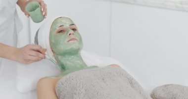 Güzellik güzel genç kız Spa prosedürleri yok. Kozmetik uzmanı bir el hasta yüz yeşil maske uygular. Vücut Bakımı sağlıklı yaşam konsepti