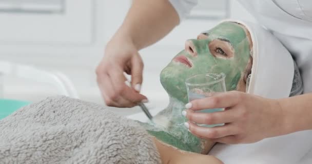 Gyönyörű fiatal lány a kozmetikus nem a gyógyfürdő eljárásokat. A nő mosott ki a zöld maszk — Stock videók