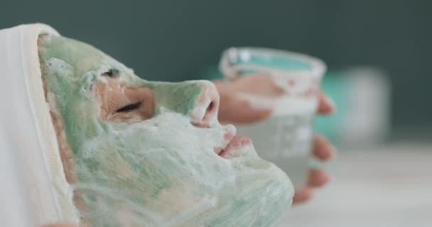 Mooie jonge meisje op de schoonheidsspecialiste doet de spa procedures. Vrouw is weggespoeld het groene gezichtsmasker — Stockvideo