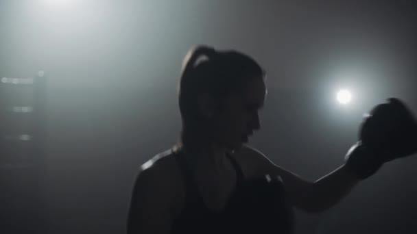 Silhouette di giovane donna che si allena con un sacco da boxe in un club di pugilato. Al rallentatore. Sfondo scuro — Video Stock