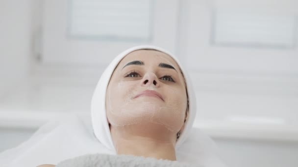 Mujer bonita joven acostada en el sofá con máscara facial blanca en el salón de belleza del spa. Movimiento lento — Vídeo de stock