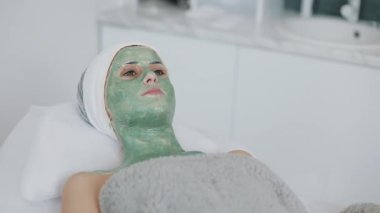 Spa salonda kadın. Yüz maskesi. Güzel kız kanepede içinde kozmetik yeşil bir maske ile yalan Kliniği. Ağır çekim.