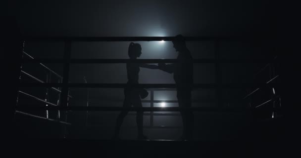 Женщина-боксер и её тренер готовятся к тренировке на боксерском ринге. Силуэт. Концепция бокса — стоковое видео