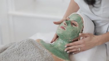 Güzel genç kız, Şevval Özçelik Güzellik spa prosedürler var. Güzellik uzmanı bir el hasta yüzünde yeşil maskesi uygular. Vücut Bakımı sağlıklı yaşam kavramı. Ağır çekim.