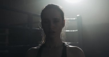 Boks halka üzerinde duran ve kameraya bakarak yorgun kadın boksör portresi