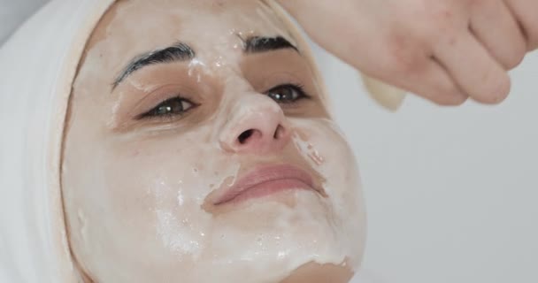 Junge hübsche Frau, die auf der Couch in der Klinik für Kosmetologie liegt. sie erhält weiße Gesichtsmaske im Wellness-Schönheitssalon — Stockvideo