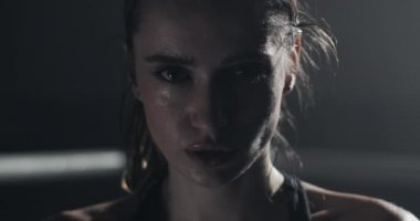 Boks halka üzerinde duran ve kameraya bakarak yorgun kadın boksör portresi