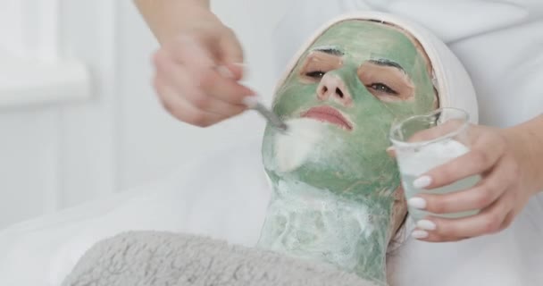 Mooie jonge meisje op de schoonheidsspecialiste doet de spa procedures. Vrouw is weggespoeld het groene gezichtsmasker — Stockvideo