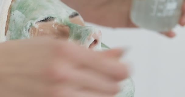 Beautiful young girl at the beautician does the spa procedures. Woman is washed off the green face mask — Stock Video