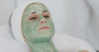 Spa salonda kadın. Yüz maskesi. Güzel kız kanepede içinde kozmetik yeşil bir maske ile yalan Kliniği
