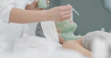 Güzellik güzel genç kız Spa prosedürleri yok. Kozmetik uzmanı bir el hasta yüz yeşil maske uygular. Vücut Bakımı sağlıklı yaşam konsepti