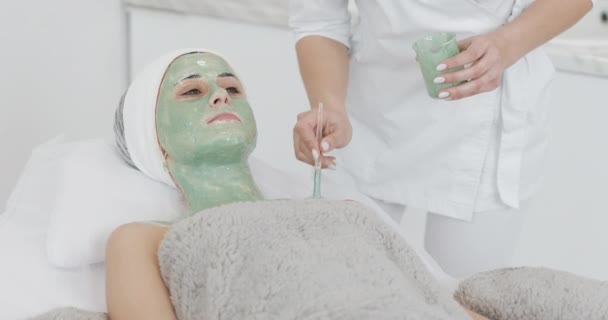 Güzellik güzel genç kız Spa prosedürleri yok. Kozmetik uzmanı bir el hasta yüz yeşil maske uygular. Vücut Bakımı sağlıklı yaşam konsepti — Stok video