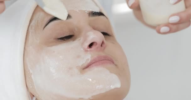 Jonge vrouw liggend op de Bank in de in cosmetologie mooie kliniek. Ze ontvangen wit gezichtsmasker in spa beauty salon — Stockvideo