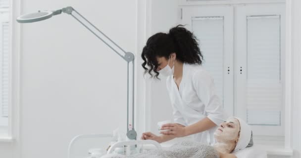 Kosmetolog sätter en vit mask på ansiktet patienten på Spa Salon. Begreppet kropps vård hälsosam livsstil — Stockvideo