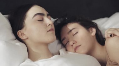 Evde yatakta kucaklayan lezbiyen çift. O uyurken bir kız başka bir kız öpüyor yavaş hareket. Lifestyle, LGBT konsepti
