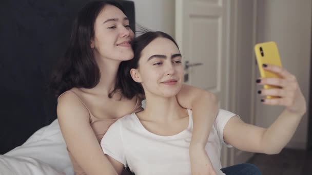 Ευτυχισμένο ζευγάρι λεσβιακό κάθεται στο κρεβάτι αγκάλιασμα και χρησιμοποιώντας smartphone λήψη selfie μαζί. ΛΟΑΤ λεσβιακό ζευγάρι μαζί. Αργή κίνηση. — Αρχείο Βίντεο