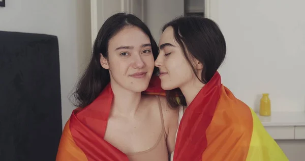 LGBT bayrağı kamera bakarak lezbiyen çift portre. İki mutlu kız evde gökkuşağı bayrağı ile poz.