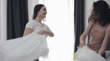Mutlu lezbiyen çift yatakta yastık mücadele sahip, eğlenceli ve gülüyor. İnsanlar, romantik ilişki ve eğlence konsepti. Yavaş hareket