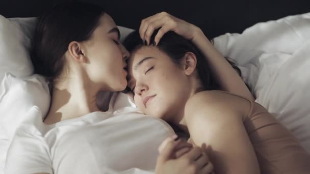 Casal lésbico abraçando na cama em casa. Uma menina beija outra garota quando ela está dormindo em câmera lenta. Estilo de vida, conceito LGBT — Vídeo de Stock