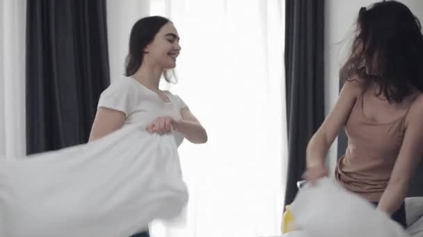 Happy lesbian couple having pillow fight on the bed, having fun and laughing. People, romantic relationship and entertainment concept. Slow motion — Stock Video