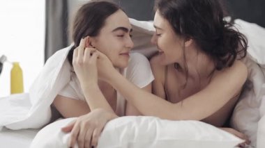 Mutlu lezbiyen çift evde battaniye altında yatakta birlikte yatarken sarılma ve Lgbt aile kavramı öpüşme. Yavaş çekim.