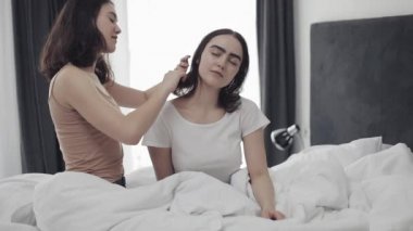 Lezbiyen kadın kız arkadaşı saç tarama. Mutlu lezbiyen çift evde yatakta oturuyor. Romantik ilişki konsepti. Yavaş çekim.