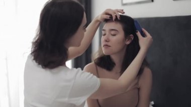 Lezbiyen kadın kız arkadaşı saç tarama. Mutlu lezbiyen çift evde yatakta oturuyor. Romantik ilişki konsepti. Yavaş çekim.
