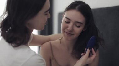 Lezbiyen kadın kız arkadaşı saç tarama. Mutlu lezbiyen çift evde yatakta oturuyor. Romantik ilişki konsepti. Yavaş çekim.