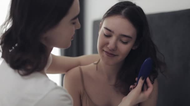 Lesbian woman combing hair her girlfriend. Happy lesbian couple sitting in the bed at home. Romantic relationship concept. Slow motion. — Stock Video